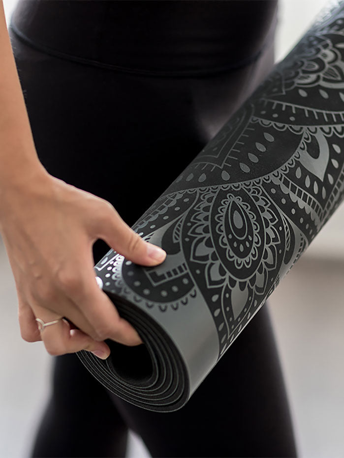 Close-up side view of a rolled-up black yoga mat with stylish mandala pattern design held by a person in yoga apparel.