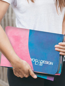 Person holding colorful pink and blue YOGA DESIGN LAB yoga mat from the side, highlighting durable texture and stylish gradient design.