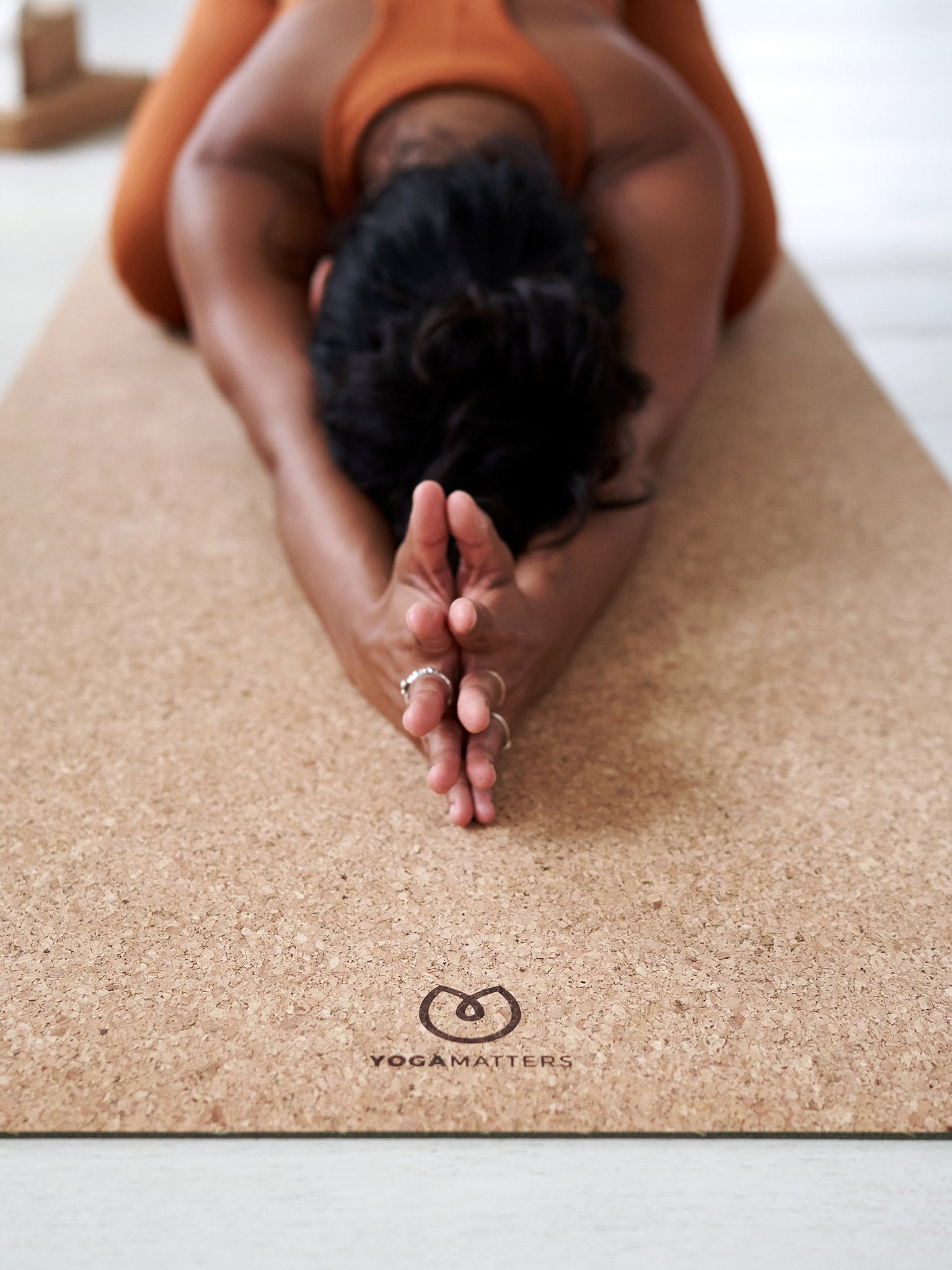Person practicing yoga on a YogaMatters cork yoga mat, demonstrating forward bend pose, shot from the front with focus on the textured surface and brand logo.
