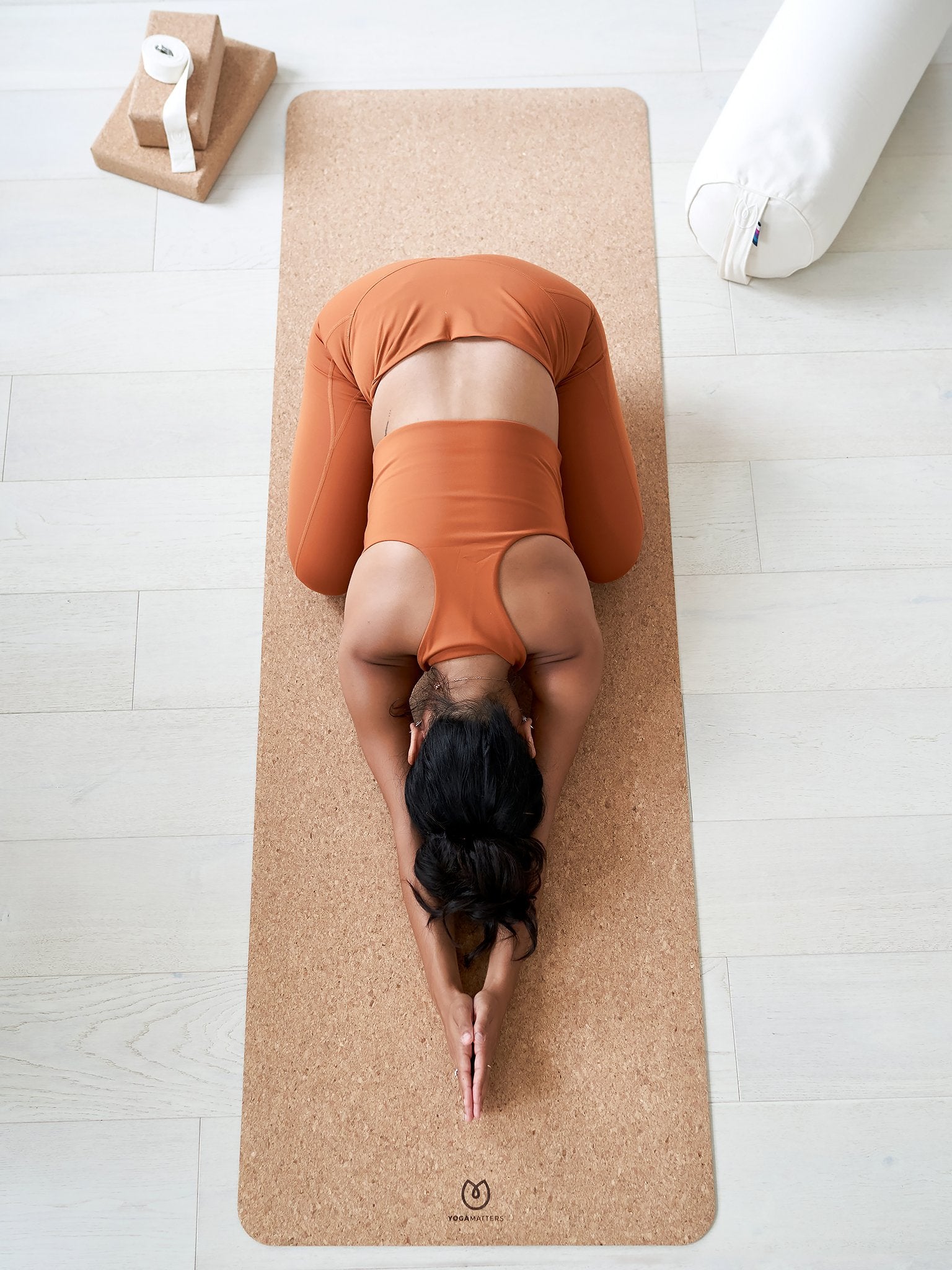 Woman practicing Child's Pose on a cork yoga mat by YOGA MATTERS, beige color, top-down view with yoga blocks and bolster, eco-friendly yoga gear, wellness and fitness concept.