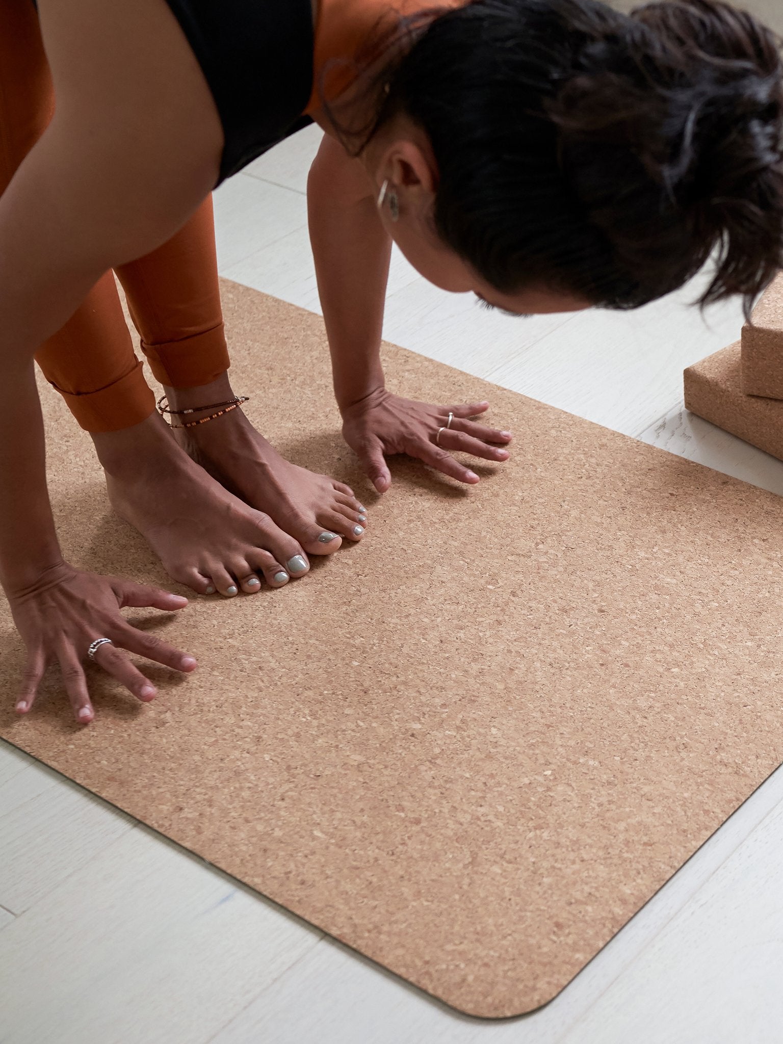 Woman practicing yoga on a textured cork yoga mat, eco-friendly non-slip surface, shot from the side with focus on hands and feet positioning, neutral tones, indoor exercise equipment