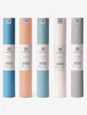 Yogamatters Eco Everyday Rise yoga mats lineup, front view, featuring multiple colors including blue, peach, light blue, and gray, textured surface, rolled for storage, with branded packaging.