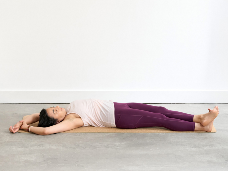 Person practising Banana Pose (Bananasana), lying on the back with the arms extended overhead and the legs and upper body curved to one side to create a crescent shape.