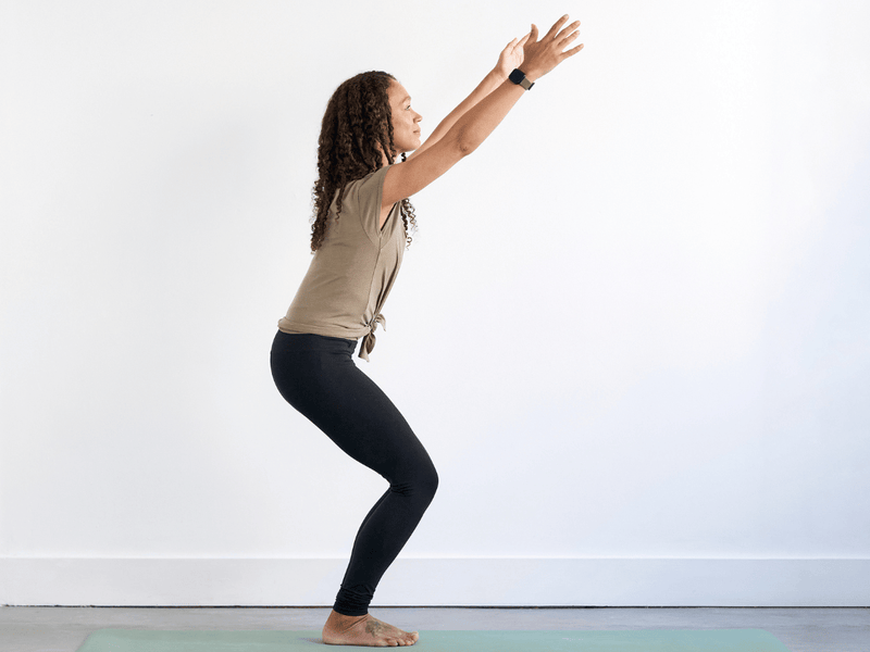 Person practising Chair Pose (Utkatasana), standing with the knees bent and hips lowered as the arms extend upwards alongside the ears.