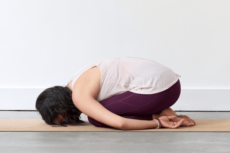 Person practising Child’s Pose (Balasana), kneeling with the hips resting towards the heels, torso folded forwards and arms extended along the body.