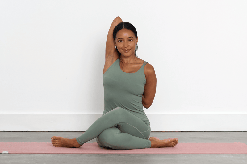 Person practising Cow Face Pose (Gomukhasana), seated with the knees stacked and arms reaching behind the back, with the hands clasped between the shoulder blades.