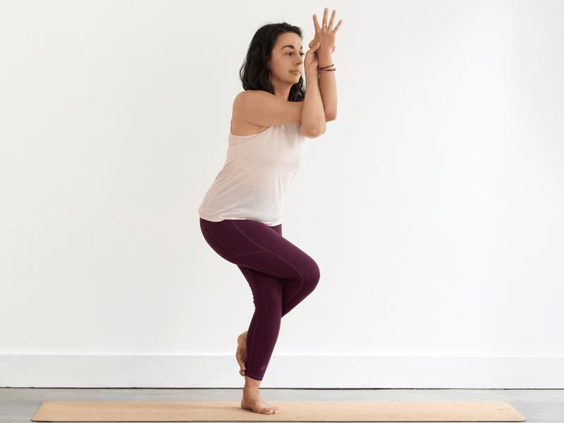 Person practising Eagle Pose (Garudasana), balancing on one leg with the opposite leg wrapped around it and the arms intertwined in front of the body.