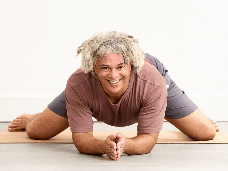 Person practising Frog Pose (Mandukasana), kneeling with the knees wide apart and lowering onto the forearms as the hips open.