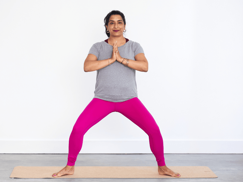 Person practising Goddess Pose (Utkata Konasana) with knees bent, feet turned out and hands together in prayer at the chest.