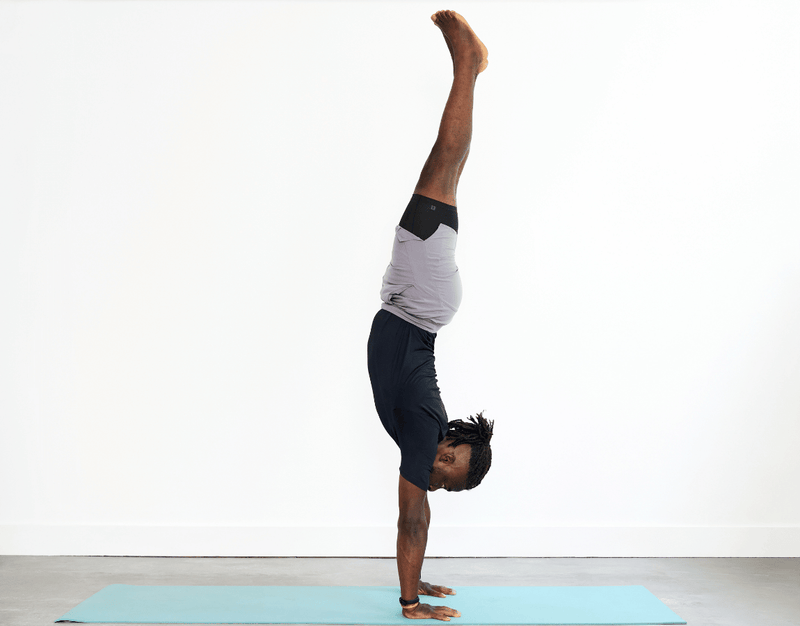 Person practising Handstand (Adho Mukha Vrksasana), balancing on both hands with the arms straight and the body and legs extending upwards.