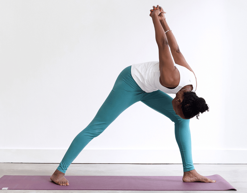 Person practising Humble Warrior Pose with the front knee bent, hands clasped behind the back and upper body folding forward inside the front leg.