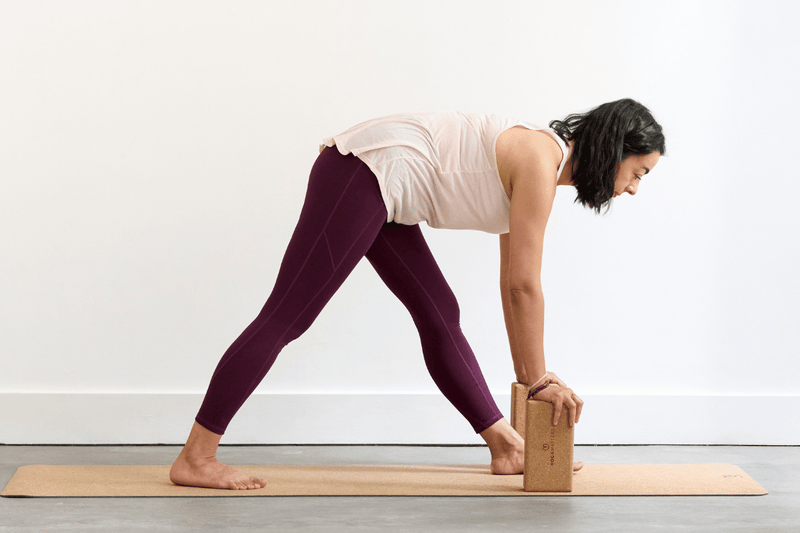 Person practising Pyramid Pose (Parsvottanasana), folding forwards over the front leg with both legs straight and the hands resting on bricks.
