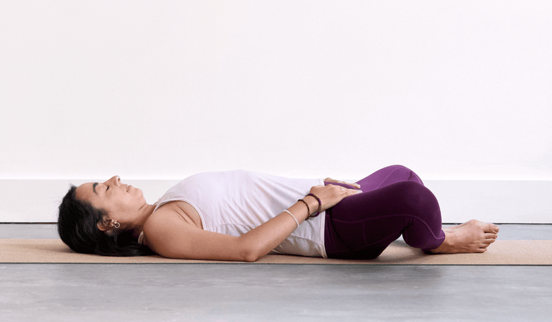Person practising Reclined Bound Angle Pose (Supta Baddha Konasana) with the soles of the feet together and knees open to the sides.