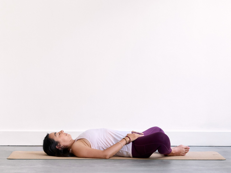 Person practising Reclined Bound Angle Pose (Supta Baddha Konasana) with the soles of the feet together and knees open to the sides.