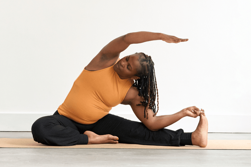 Person practising Revolved Head-to-Knee Pose (Parivrtta Janu Sirsasana), extending one leg to the side and reaching the upper arm overhead towards the extended foot in a deep side bend.