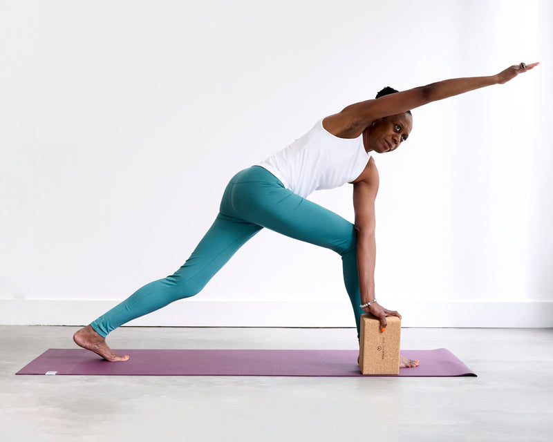 Person practising Revolved Side Angle Pose (Parivrtta Parsvakonasana), twisting over the front leg with one hand grounded on a brick and the opposite arm reaching upwards.