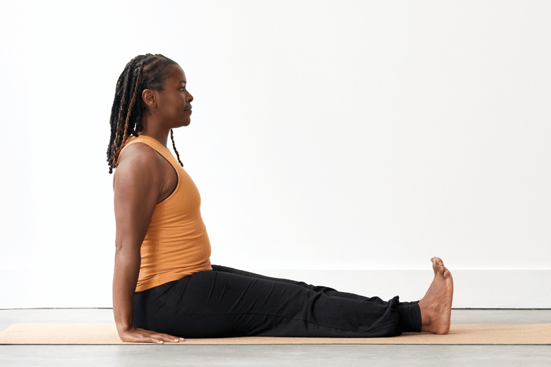 Person practising Staff Pose (Dandasana), sitting upright with legs extended straight in front and hands resting on the floor beside the hips.