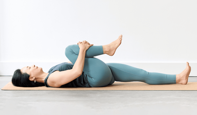 Person practising Half Wind-Relieving Pose (Ardha Pavanamuktasana), lying on the back with one knee drawn towards the chest and the opposite leg extended along the mat.