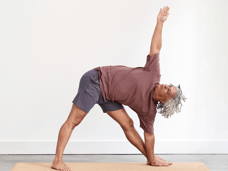 Person practising Triangle Pose (Trikonasana), standing with the legs wide and straight, with the bottom hand reaching towards the floor and the opposite arm extending upwards.