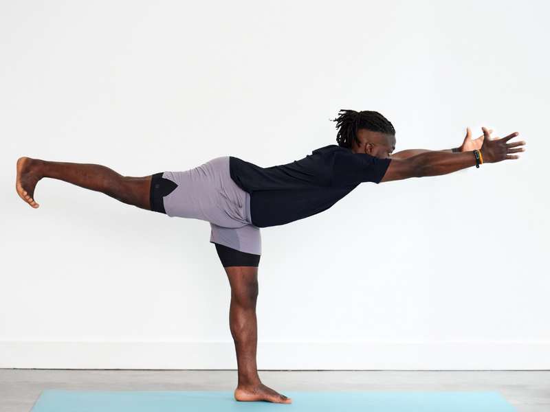 Person practising Warrior III (Virabhadrasana III), balancing on one leg with the opposite leg extended behind and the upper body reaching forwards, creating a long line through the body.