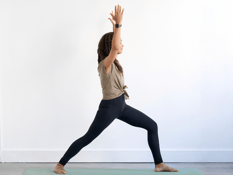 Person practising Warrior I (Virabhadrasana I) with the front knee bent, back foot grounded and arms extended overhead.