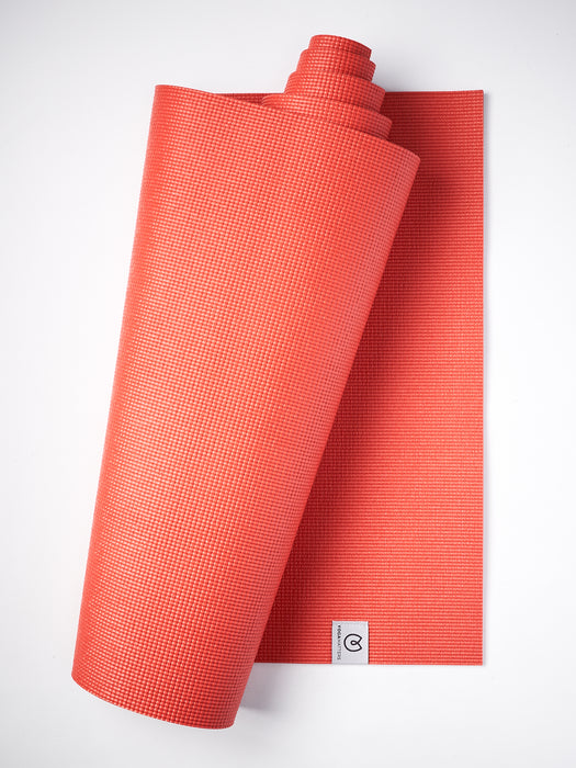 Red textured non-slip yoga mat partially rolled up with visible brand logo, photographed from the side on a white background.