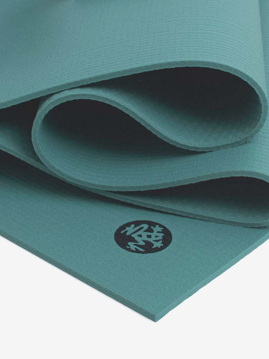 Teal yoga mat partially rolled displaying textured surface and circular logo, close-up side view for yoga accessories.