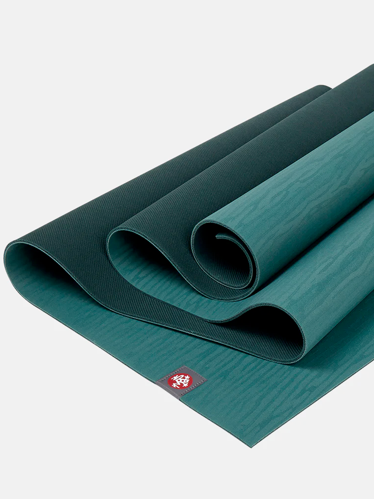 Green Manduka PRO yoga mat rolled up on white background showing texture and brand logo