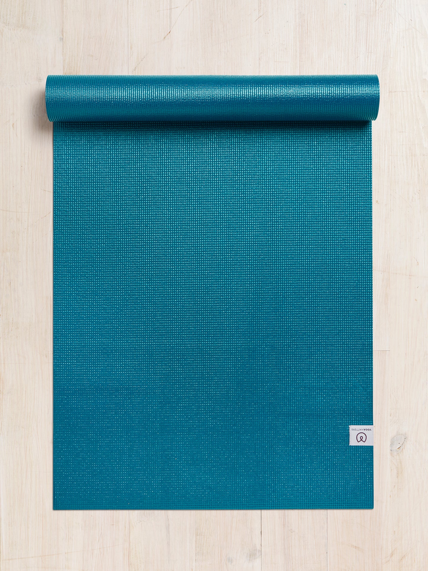 Teal textured yoga mat partially rolled up, top view on a wooden floor, eco-friendly high-grip exercise mat with visible brand logo