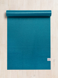 Teal textured yoga mat partially rolled up, top view on a wooden floor, eco-friendly high-grip exercise mat with visible brand logo