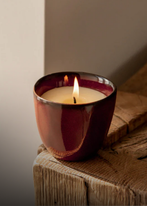 Candle in a red holder on a wooden surface with a neutral background