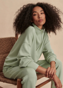 Woman in a light green outfit sitting on a chair against a beige background