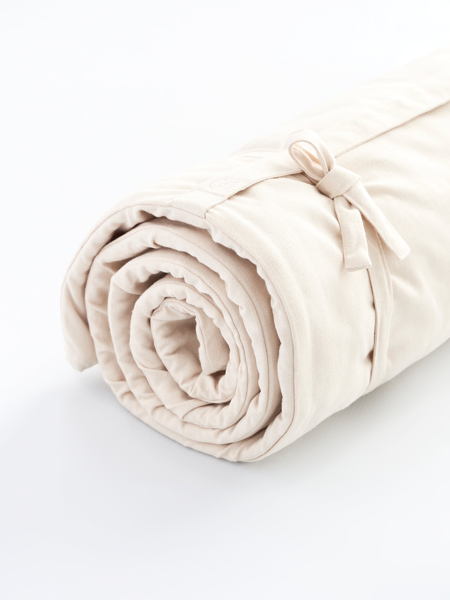 Beige rolled yoga mat side view with strap detail on white background