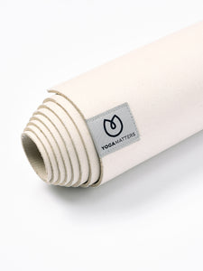 Yogamatters rolled up eco-friendly natural color yoga mat with brand tag visible, textured non-slip surface, close-up side view on a white background.