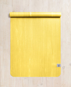 Bright yellow yoga mat by Lululemon with textured surface, rolled up at the top, photographed from above on a light wooden floor