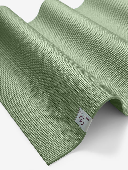 Green textured yoga mat with visible brand logo, rolled half-way, angled side shot, non-slip exercise mat for fitness and meditation.