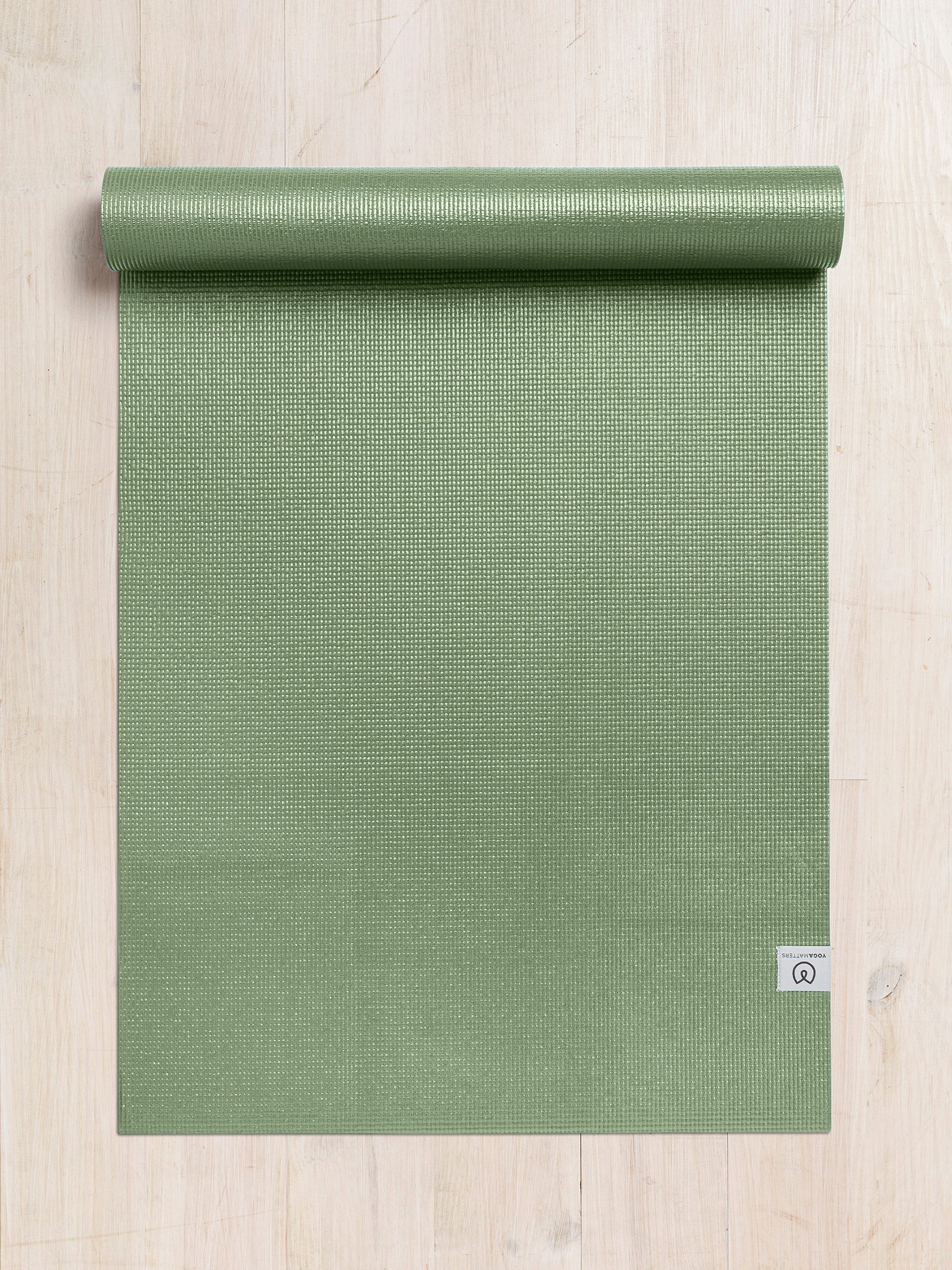 Green textured yoga mat partially rolled from top on wooden floor, top view, non-slip surface, exercise and wellness accessory