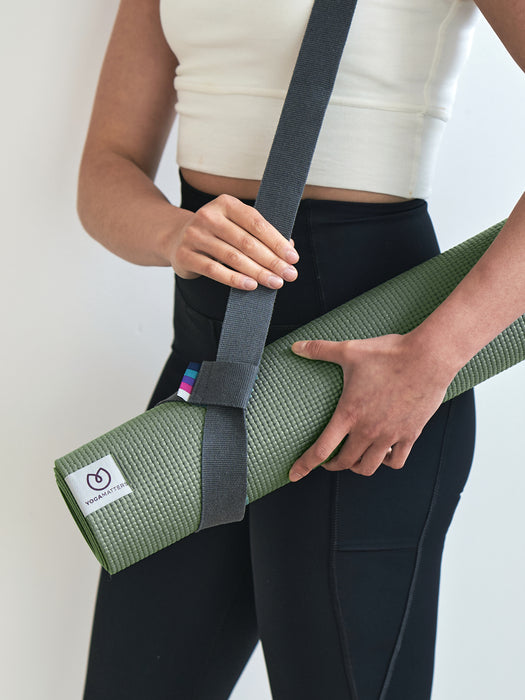 Woman holding a rolled-up YogaMatters olive green yoga mat with gray carrying strap, eco-friendly textured design, side shot with focus on mat and strap detail.