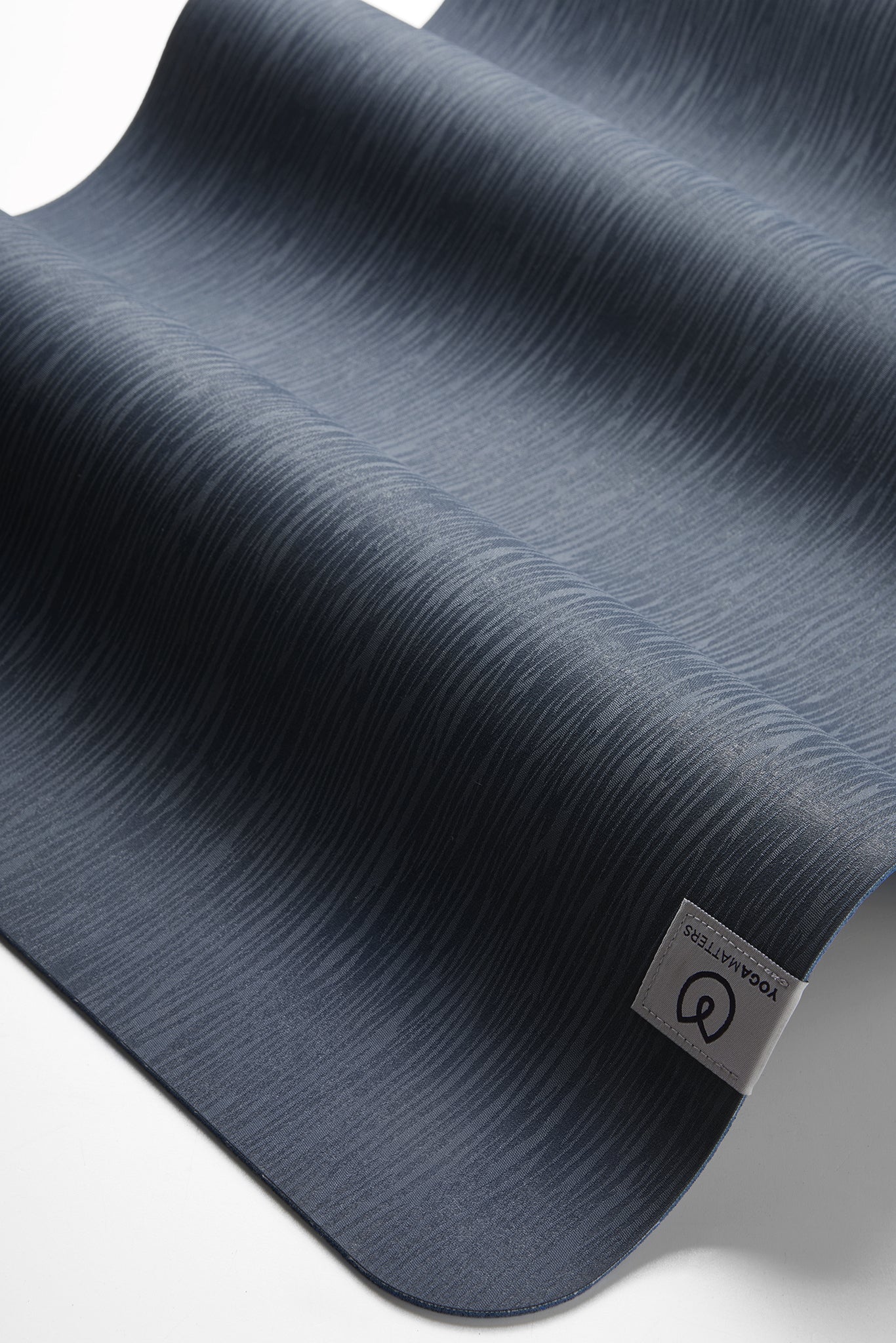 Lululemon yoga mat in navy blue, close-up side view, textured non-slip surface, rolled halfway for product detail display