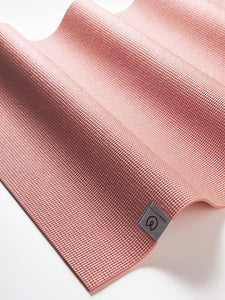 Close-up of a textured coral pink yoga mat from a side angle with visible brand logo