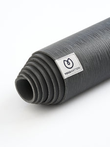 Rolled dark grey YogaMatters yoga mat side view with visible brand label on a white background