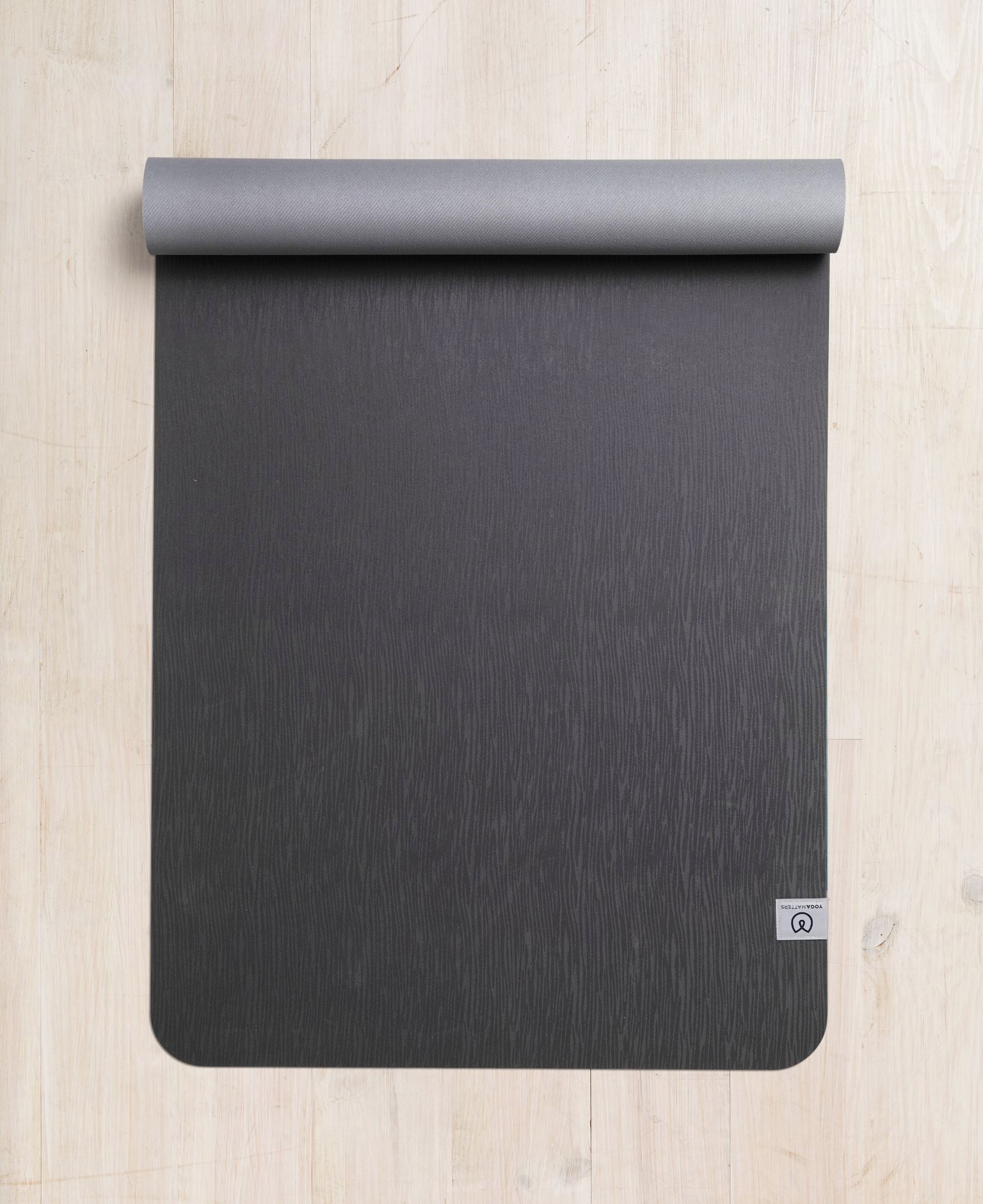 Top view of a rolled dark gray yoga mat with textured design on a wooden floor, eco-friendly materials, non-slip surface, fitness and wellness accessory.