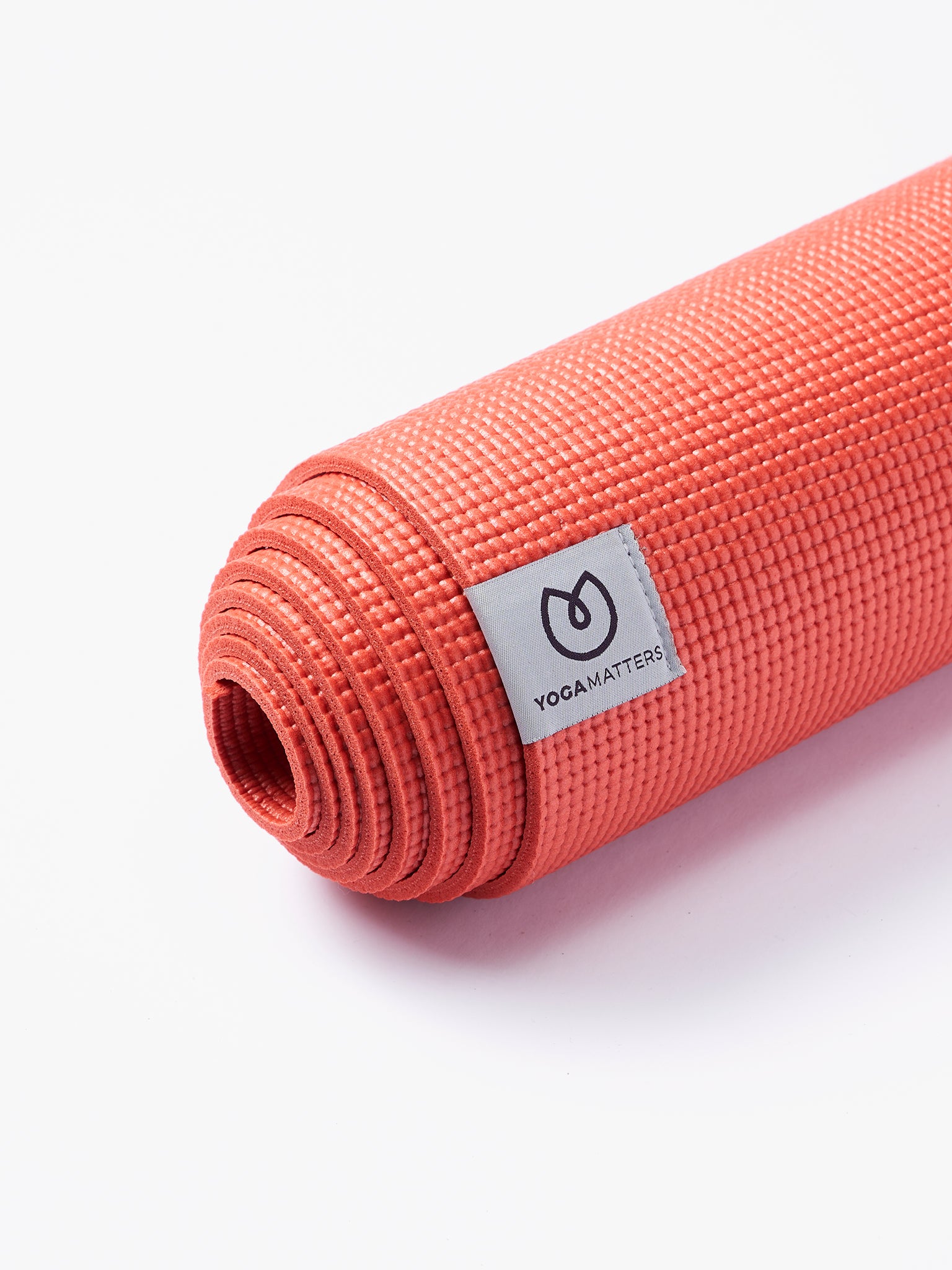 Coral red YogaMatters yoga mat rolled up side view with textured surface on a white background