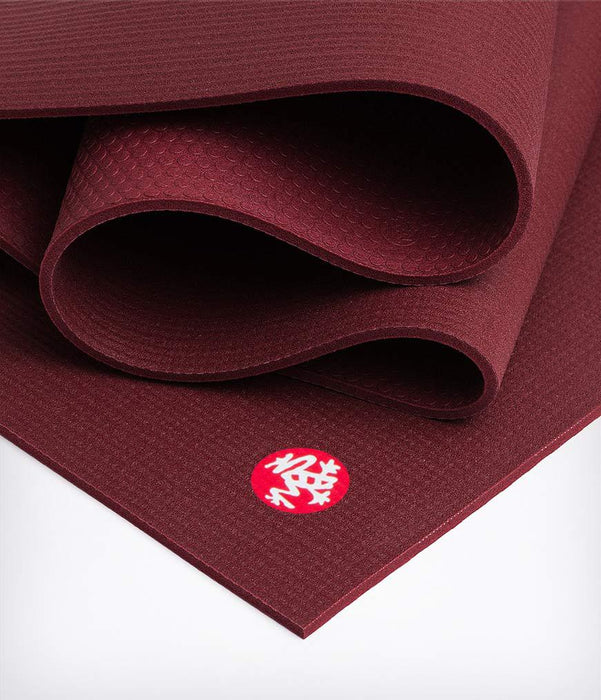 Burgundy yoga mat with textured surface, partially rolled, angled side view showing logo