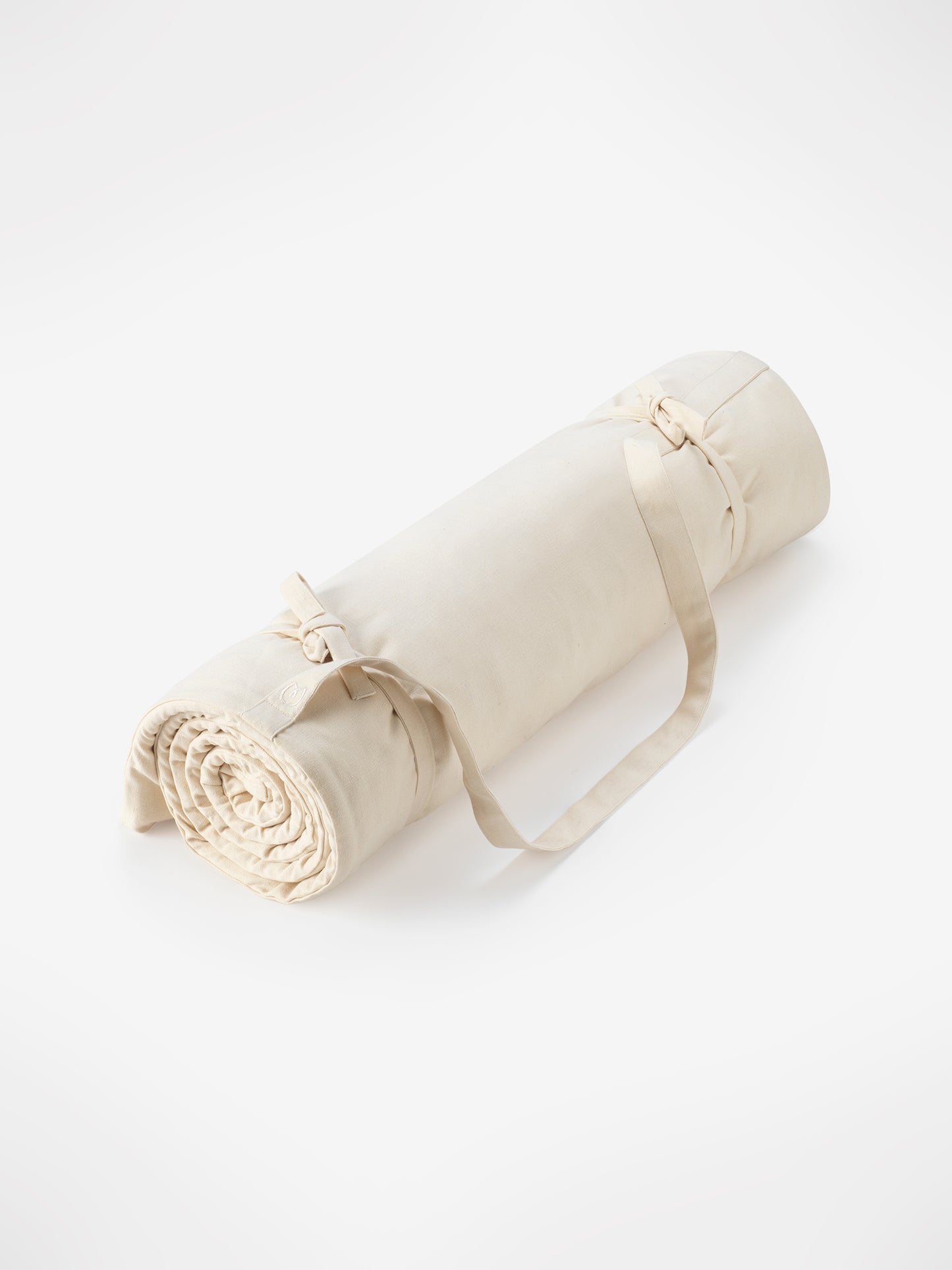 Beige yoga mat rolled up with straps on white background, non-slip surface, eco-friendly material, portable design, high-quality exercise and fitness accessory, side angle view.