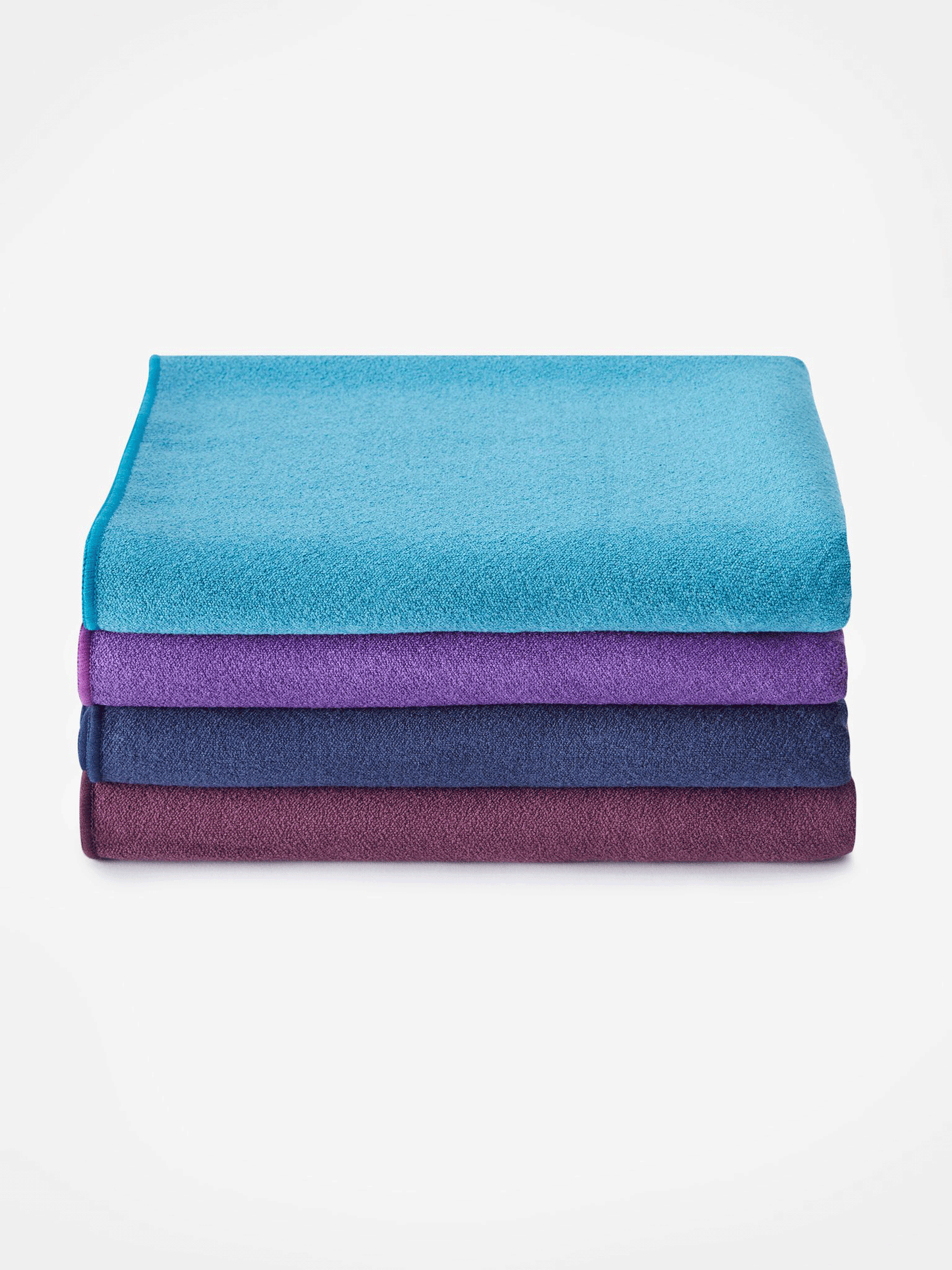 Stack of three rolled yoga mats from top view in blue, purple, and burgundy colors, textured non-slip surface, isolated on white background.