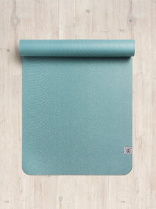 Teal yoga mat partially rolled up on wooden floor shot from above with visible textured surface and logo in the bottom right corner
