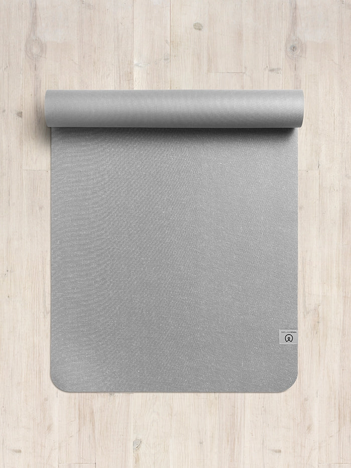 Top view of a rolled gray yoga mat on a wooden floor.