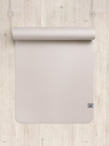 Non-slip beige yoga mat partially rolled out on wooden floor with visible logo, top view fitness equipment photography.