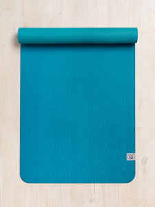 Teal yoga mat with textured surface partially rolled out on wooden floor, top-down view, with visible brand logo.